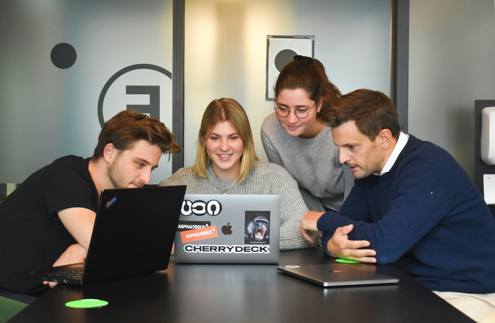 Four people gathered around one laptop at a table, working through a problem together