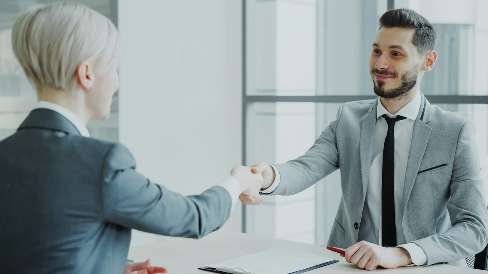 Two people shaking hands across a desk — the scope conversation, not the demo, is where a first client is won